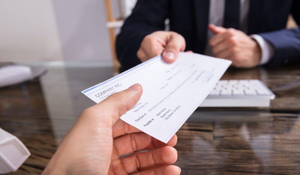 Close-up,Of,A,Businessperson's,Hand,Giving,Cheque,To,Colleague,At